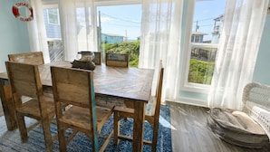 A dining area with a wooden table and chairs, a rug, and a view of the outdoors. - ☀️Newly renovated cottage at the coast….60 second walk to the beach🌊 (North Topsail Beach)