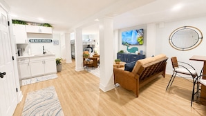 A modern living room with a sofa, a dining table, and a kitchen area with white cabinets. - ☀️Newly renovated cottage at the coast….60 second walk to the beach🌊 (North Topsail Beach)