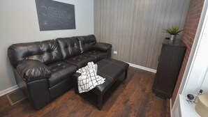 Un salon avec un canapé en cuir foncé, un pouf assorti et une carte murale.