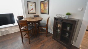 Un coin repas comprenant une table ronde en bois, quatre chaises, un téléviseur et deux œuvres d’art encadrées accrochées au mur.