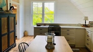 A kitchen with white cabinets, a wooden table, and a window with a view of greenery.