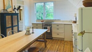 A kitchen with wooden beams, a large window, a stove, and a dining table.