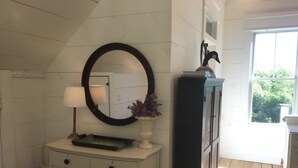 A bathroom with a white vanity, a mirror, a lamp, and a window with a view of greenery.