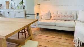 A cozy living room with a wooden dining table, a white sofa with patterned cushions, and a white cabinet with a sink.