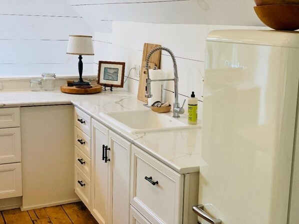A kitchen with white cabinets, a sink, a faucet, a lamp, and a refrigerator.