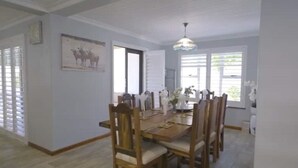 A dining area with a wooden table and chairs, a chandelier, and a window with blinds. - Mount View. Luxury 3 bed villa with pool (Cape Town)