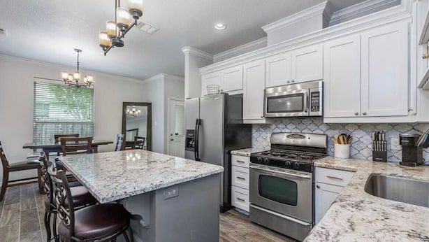 A modern kitchen with white cabinets, granite countertops, stainless steel appliances, and a central island with bar stools.
