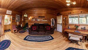 A cozy cabin interior with a wooden interior, a fireplace, a dining area, and a bookshelf.