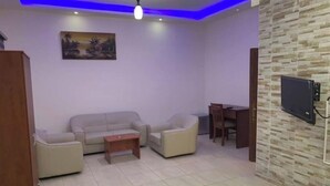 A modern living room with a sofa set, a small table, a TV mounted on the wall, and a ceiling light. - @ECONOMY APARTMENT@ 104 (Amman)