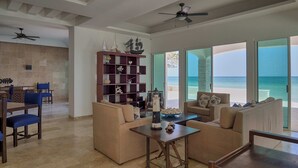 A spacious living area with a view of the ocean, a wooden bookshelf, and a dining area with blue chairs. - Casa Mega - Yucatan Home Rentals (Chicxulub Puerto)