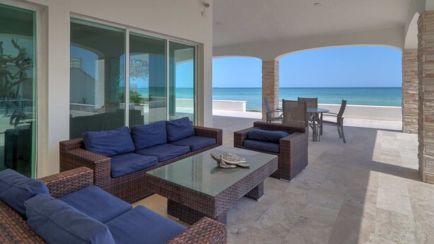 A covered outdoor seating area with wicker furniture and a glass coffee table, overlooking a beach. - Casa Mega - Yucatan Home Rentals (Chicxulub Puerto)