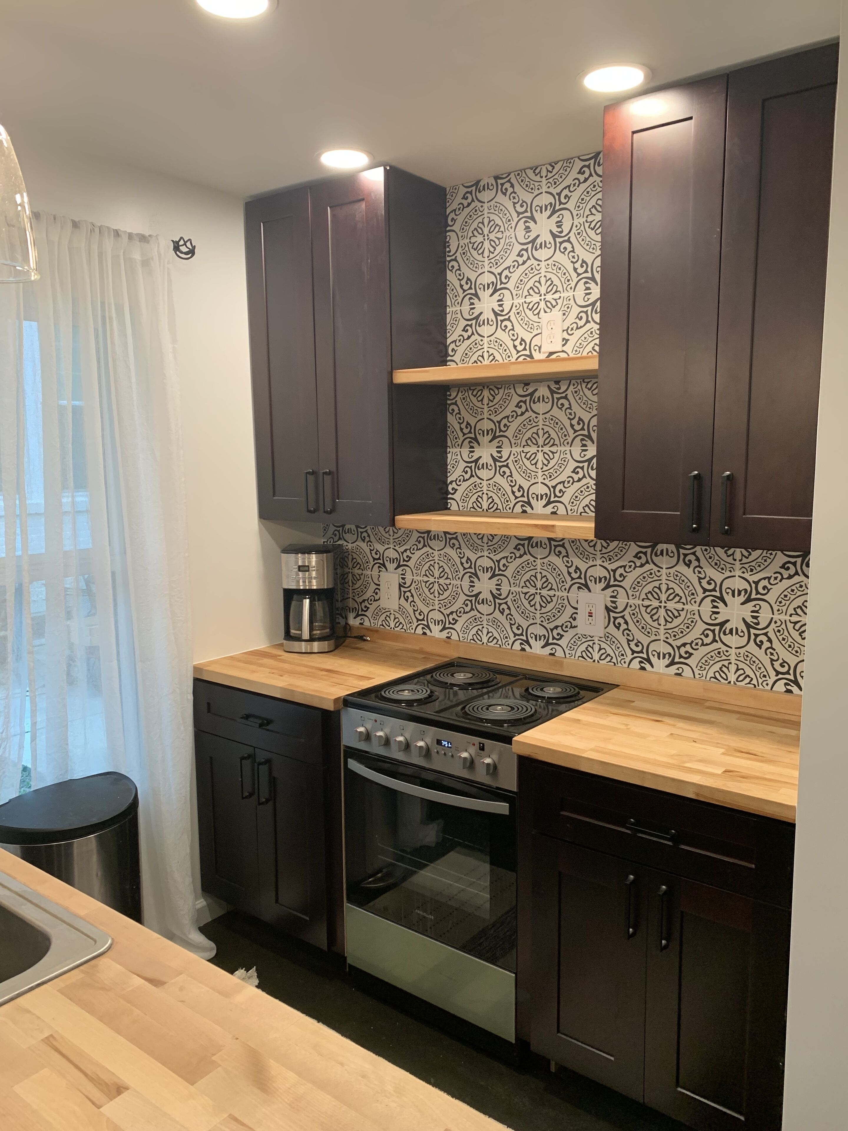 A modern kitchen with dark wooden cabinets, a stainless steel stove, and a patterned backsplash.