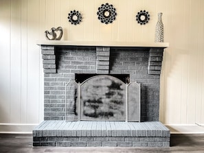 Cozy room features a warm fireplace with a brick facade and metal screen, complemented by decorative wall art and a vase.