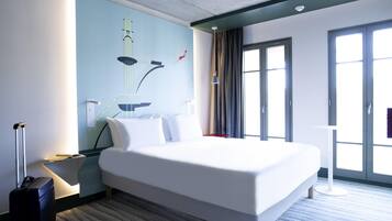 Une chambre d’hôtel avec un grand lit, un bureau, une valise, une œuvre d’art accrochée au mur et une fenêtre avec des rideaux.