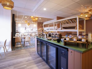 A hotel breakfast area with a counter, seating, and a view of the dining area. - ibis Styles Le Touquet (Le Touquet-Paris-Plage)