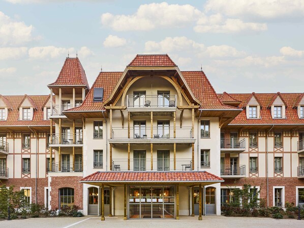 Un hotel de varios pisos con un estilo arquitectónico europeo tradicional, que cuenta con un atrio central, balcones y un tejado de tejas rojas.