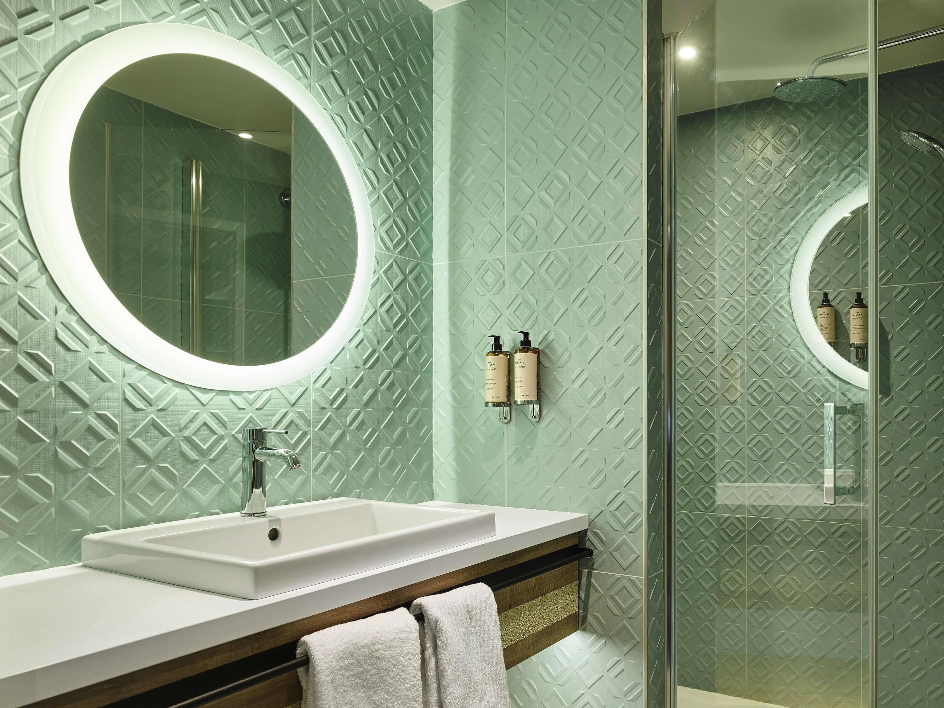 Une salle de bain avec un miroir rond, un lavabo et un espace douche.