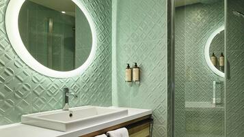 Une salle de bain avec un miroir rond, un lavabo et un espace douche.