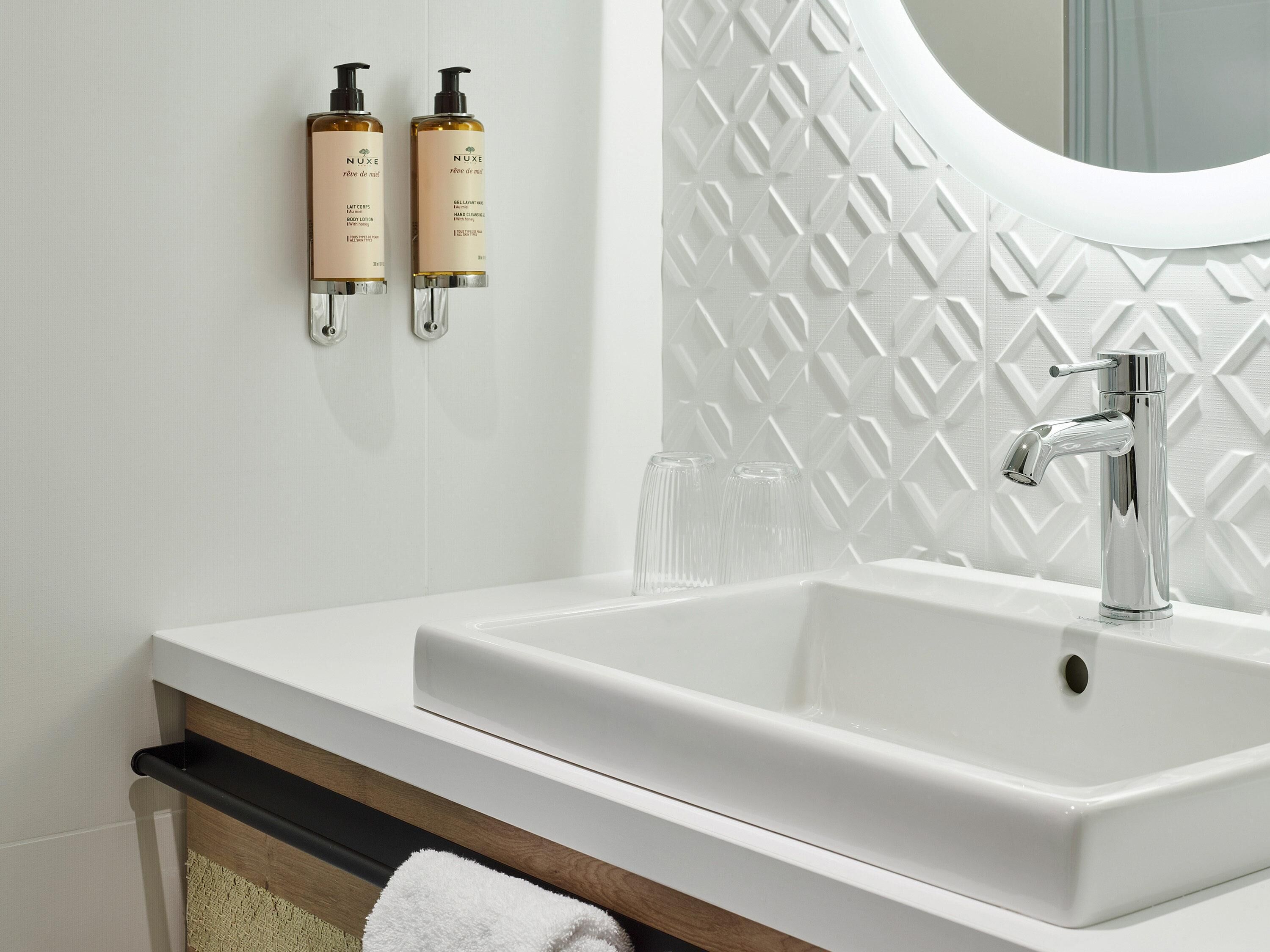 Une salle de bain avec un lavabo blanc, un miroir et deux flacons de lotion accrochés au mur.