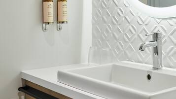 Une salle de bain avec un lavabo blanc, un miroir et deux flacons de lotion accrochés au mur.