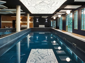 En moderne indendørs swimmingpool med et mønstret gulv, store vinduer og et loft med geometrisk design.