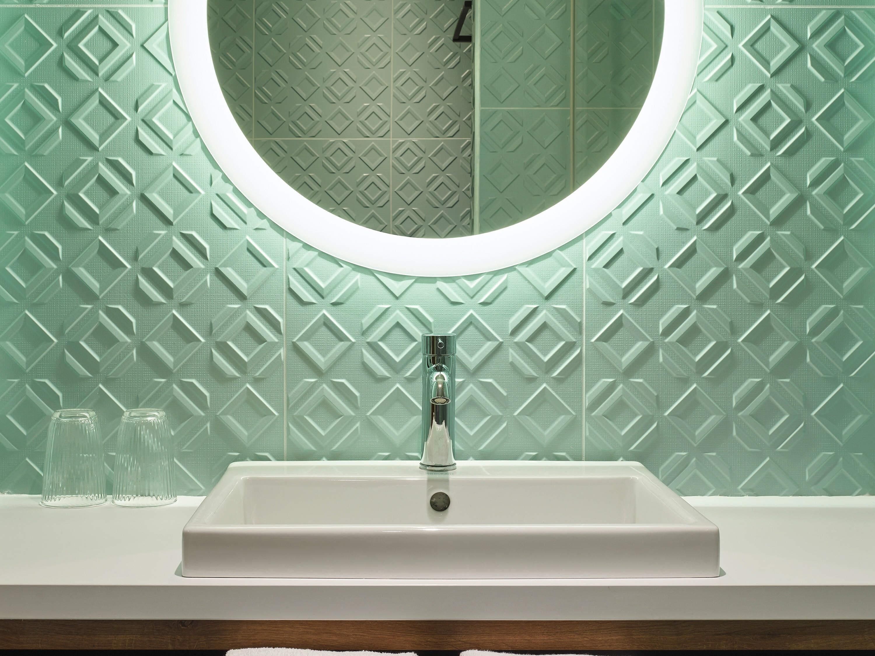 Un baño con un lavamanos blanco, un espejo redondo y un papel tapiz con diseño de diamantes.