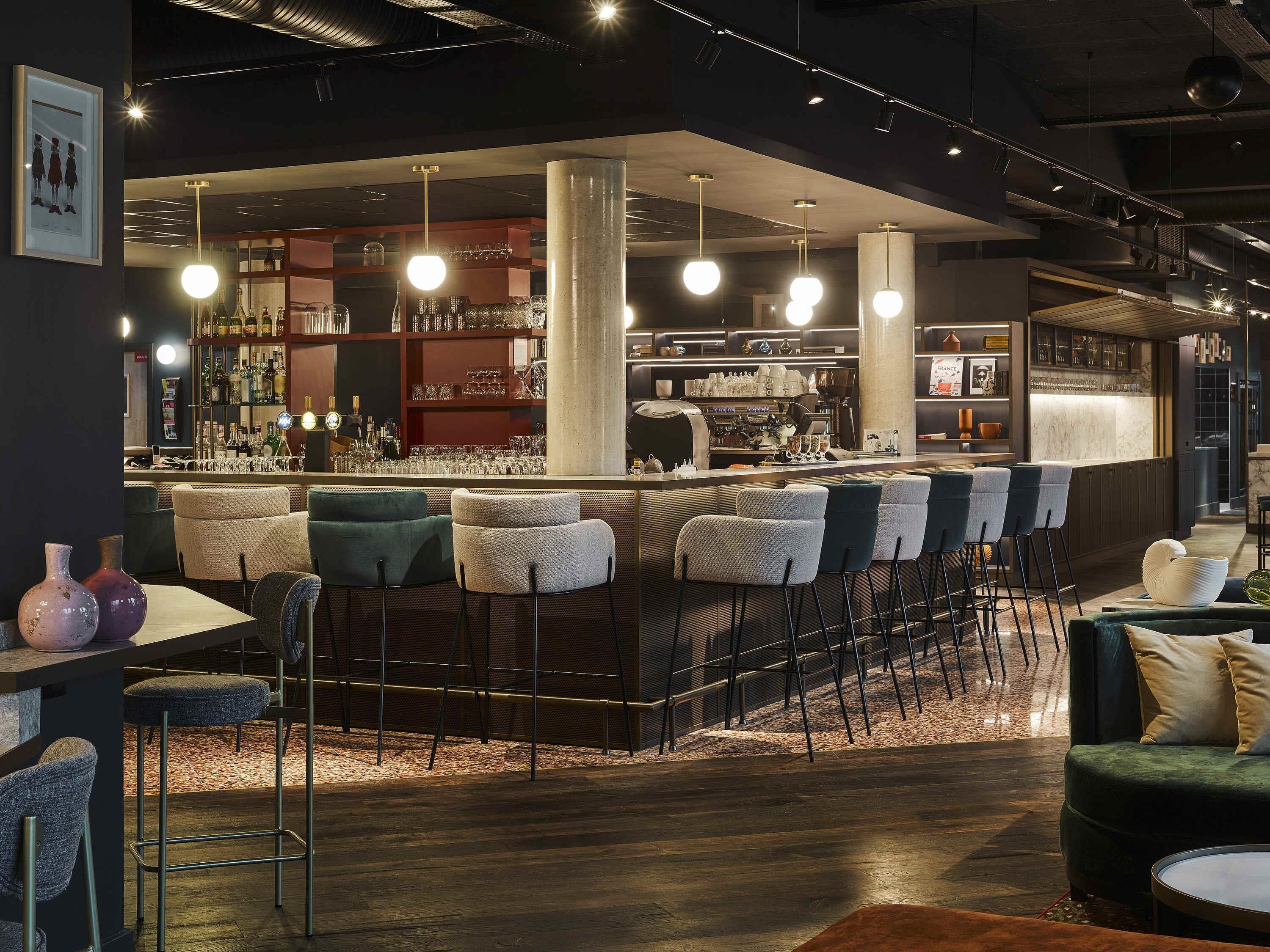 A modern bar area with a bar counter, multiple stools, and a seating area with a sofa and chairs.