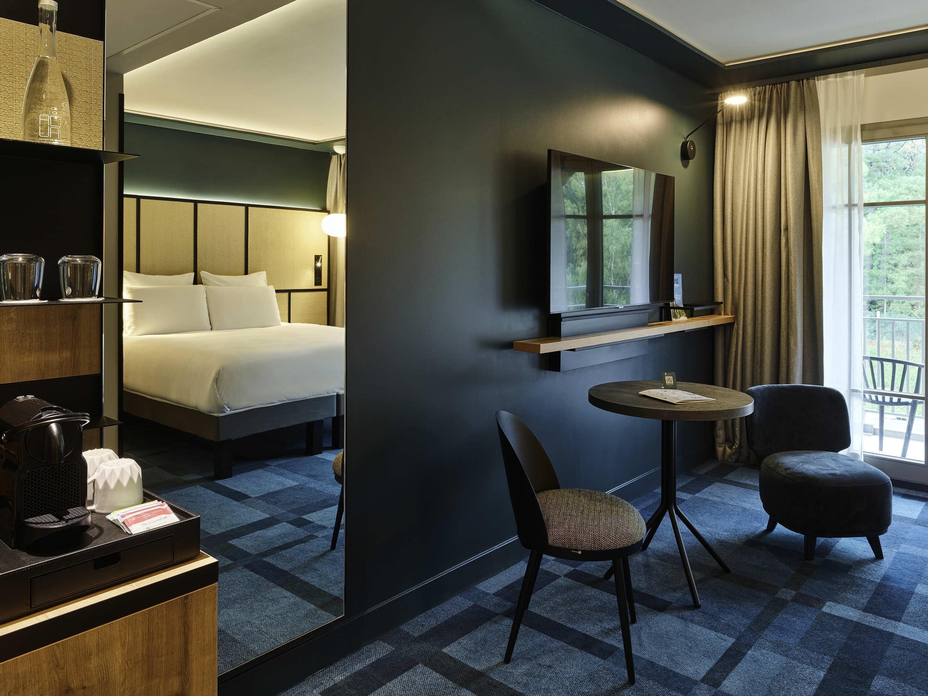 Une chambre d’hôtel avec un lit, un bureau et une chaise, une télévision et une fenêtre avec des rideaux.