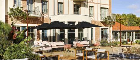 Un hotel con mesas al aire libre, que incluye sofás y sillones, y un patio cubierto.