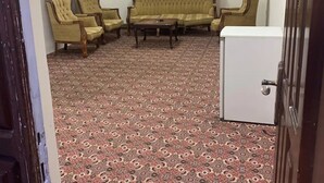 Quarto com carpete estampado, um sofá, duas poltronas, uma mesa de centro e um armário branco.