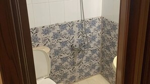Casa de banho com sanita, chuveiro e azulejos com padrão floral.