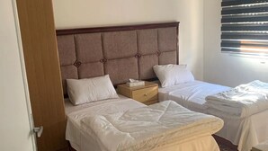 Quarto de hotel com duas camas, uma cabeceira de madeira, uma mesa de cabeceira e uma janela com persianas.