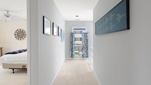A hallway with a bed, framed pictures, and a ceiling fan. - Serene Sunrise & Shimmering Skyline. 5 Star Hosts (Ocean City)