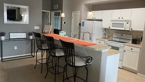 Una cucina moderna con isola centrale, sgabelli da bar, mobili bianchi e un forno a microonde.