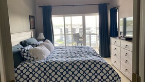 Camera da letto con un letto grande, una cassettiera, una TV e un balcone con vista sugli edifici.