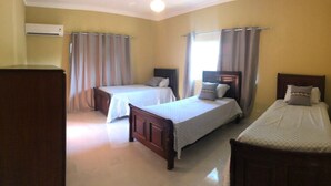 Una habitación de hotel con tres camas individuales, un armario de madera y una ventana con cortinas.