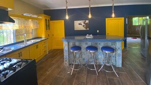 Una cocina con armarios amarillos, una isla azul con taburetes y una lámpara colgante.