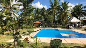 Un área de piscina con palmeras, una carpa blanca y un edificio pequeño con techo rojo.