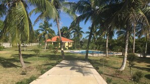 Un camino que lleva a una zona de piscina con palmeras y un edificio de techo rojo.