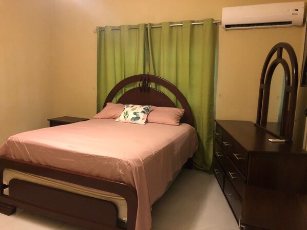 A bedroom with a bed, a dresser, a mirror, and an air conditioning unit.