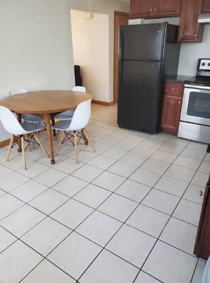A kitchen with a dining table, chairs, a refrigerator, and an oven.