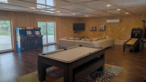 Una mesa de billar en una sala con paredes de madera, un sofá y juegos de arcade.