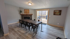 Un comedor amplio con una larga mesa y sillas, chimenea y vistas al exterior.