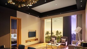 Een moderne hotelkamer met een groot raam, een flatscreen televisie, een eethoek en een zithoek met uitzicht op palmbomen.