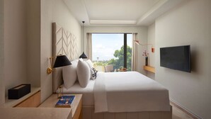 Een moderne hotelkamer met een groot bed, een flatscreen televisie, een bureau met een lamp en uitzicht op de stad.