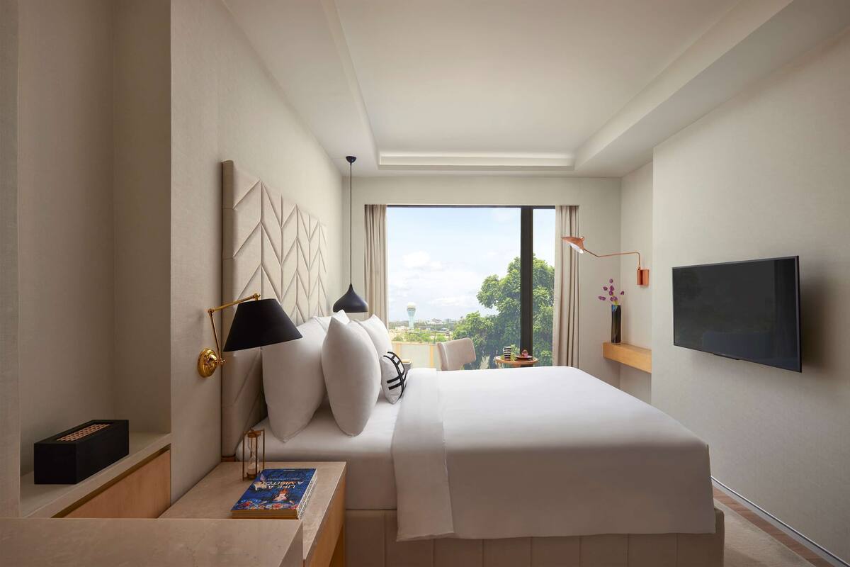 Ein modernes Hotelzimmer mit einem großen Bett, einem Flachbildfernseher, einem Schreibtisch mit Lampe und Blick auf die Stadt.