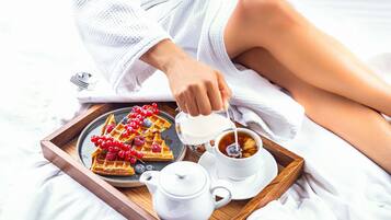 Una bandeja con waffles cubiertos de frutos rojos, una taza de té y una tetera sobre la cama.
