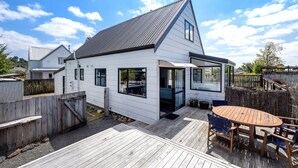 A white house with a sloped roof, a deck with a table and chairs, and a wooden fence. - Sparkling 3-bedroom home with fireplace and views (National Park)