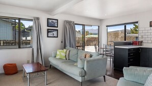 A modern living room with a sofa, a small table, and a kitchen area with a counter and cabinets. - Sparkling 3-bedroom home with fireplace and views (National Park)