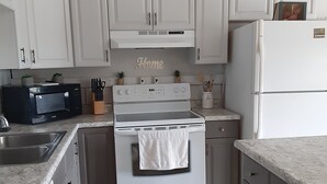 A kitchen with white cabinets, a stove, a microwave, and a refrigerator. - Cozy Mountain View Retreat (Brighton)